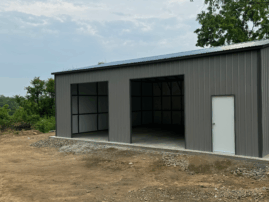 Pewter gray metal garage with two open bays, a white walk-in door, and vertical siding, installed in Albert Lea, Minnesota by American Steel Carports, Inc.