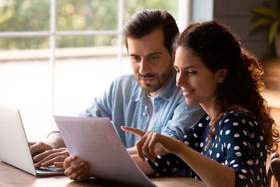 A man and woman examine a document on a laptop, focused on financing a custom steel workshop in Oklahoma.